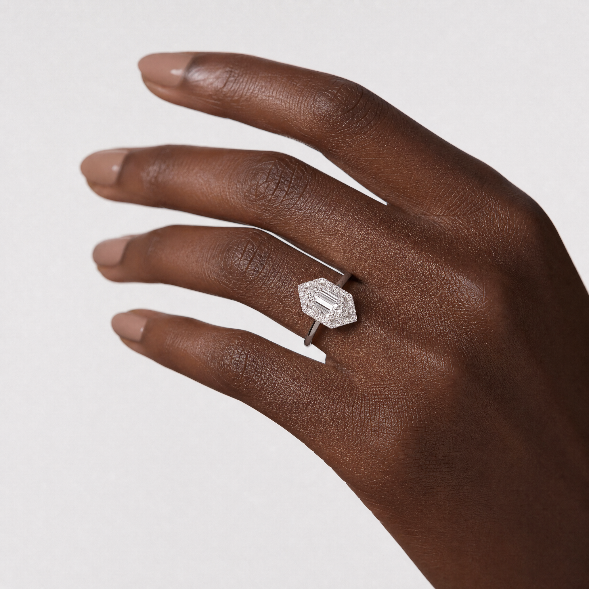 close up a hand wearing a 18K  hexagon halo diamond ring  against a light gray background