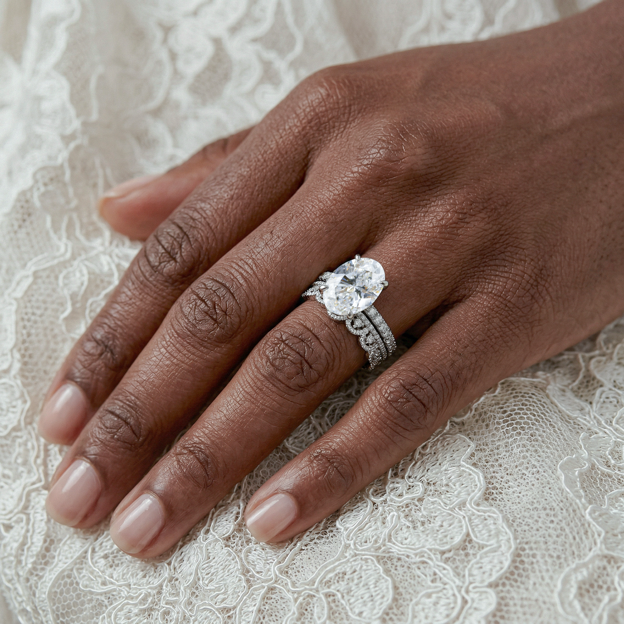 Hand wearing  oval diamond ring with band on a lace background