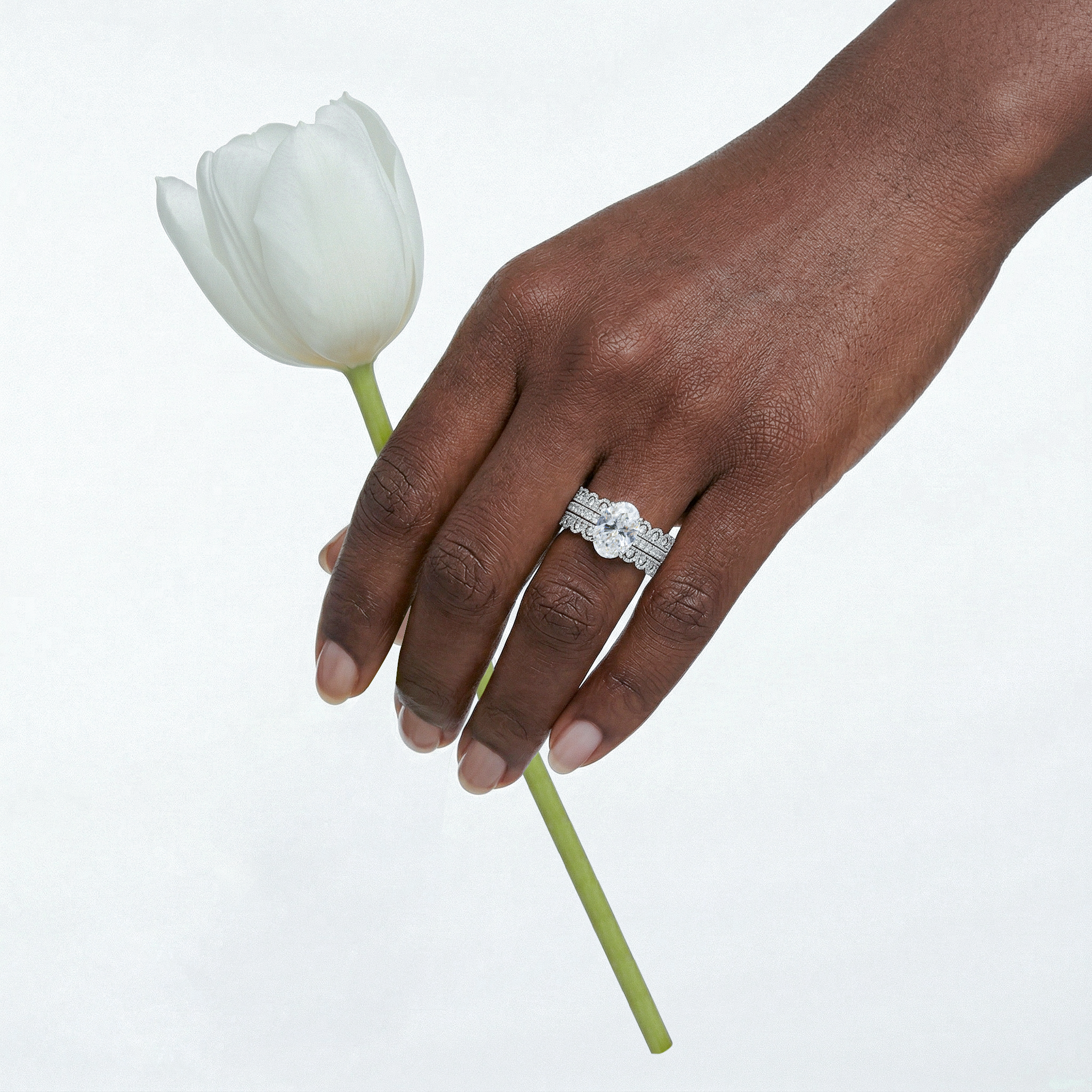 Hand holding a white tulip with a white gold oval diamond ring set