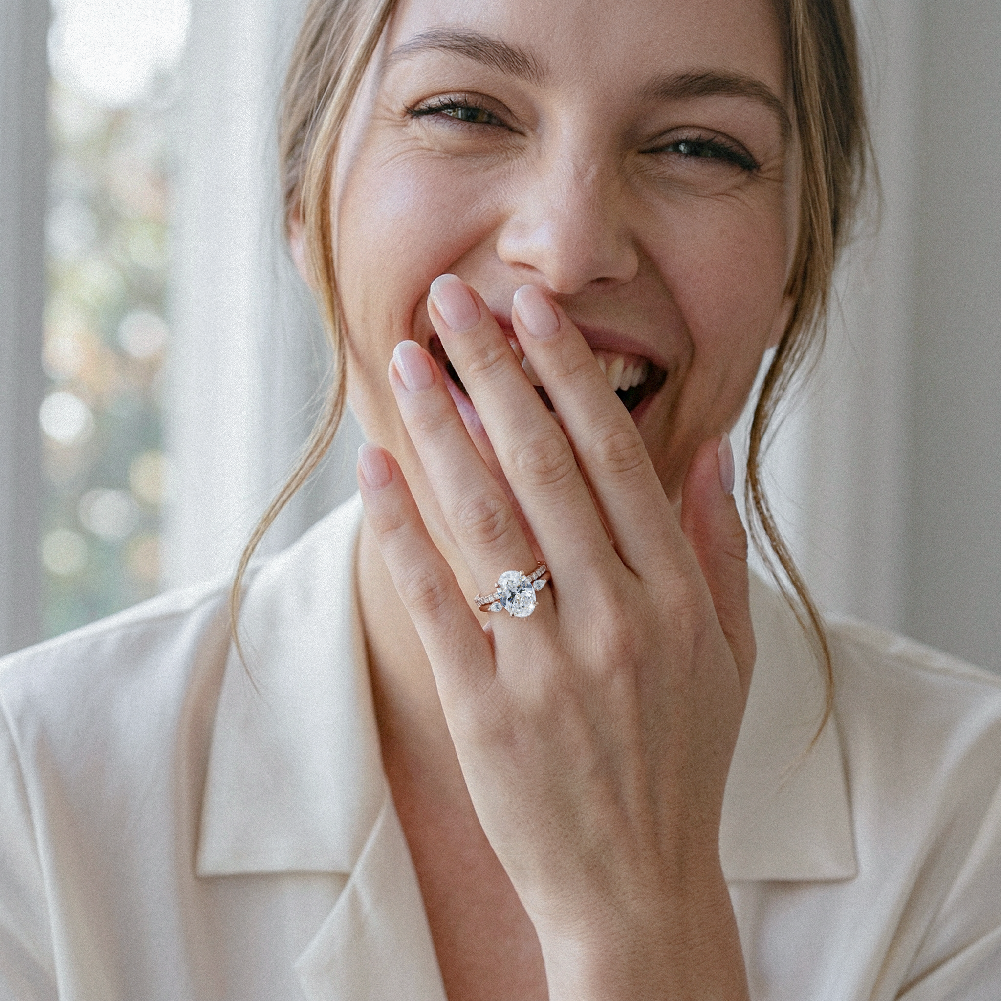 Woman wearing a diamond ring, smiling with hand covering mouth.