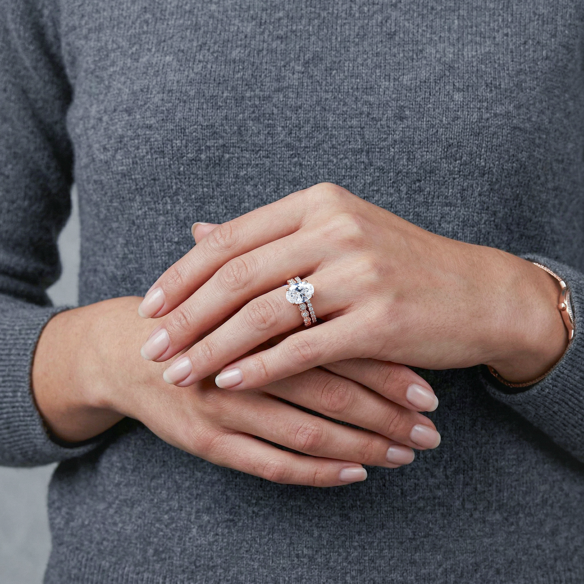 Close-up of hands with rose gold  oval diamond ring set  on a gray background
