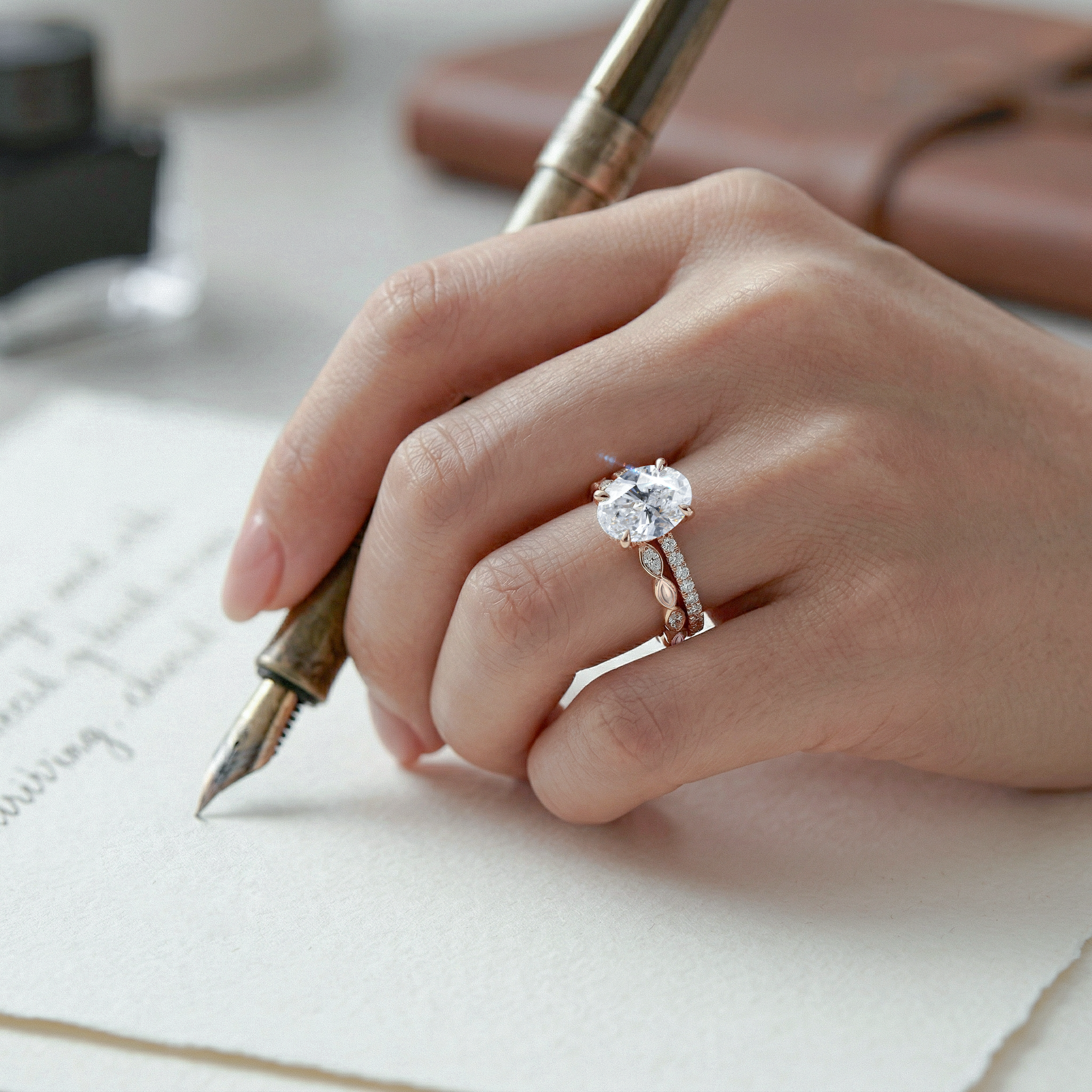Hand with oval ring set diamond ring holding a fountain pen over a piece of paper.