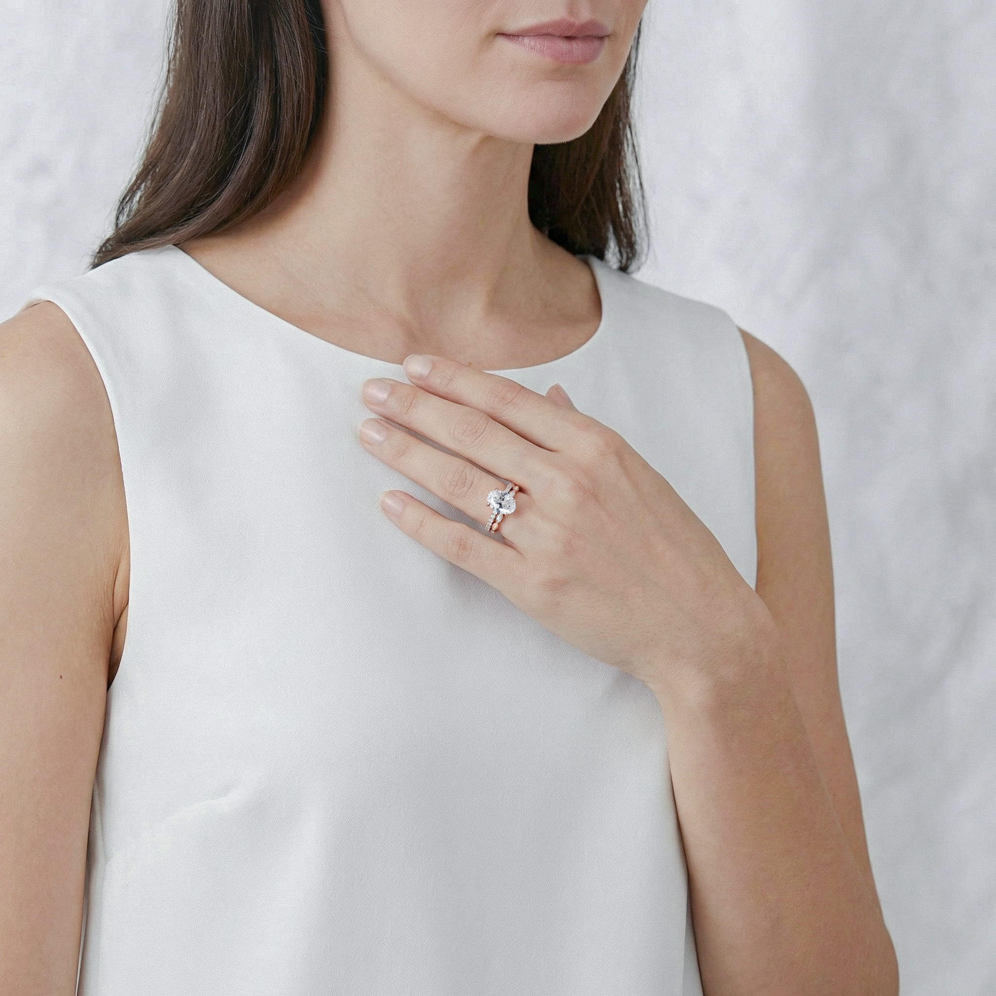 Woman wearing a gold oval diamond ring set on a plain background