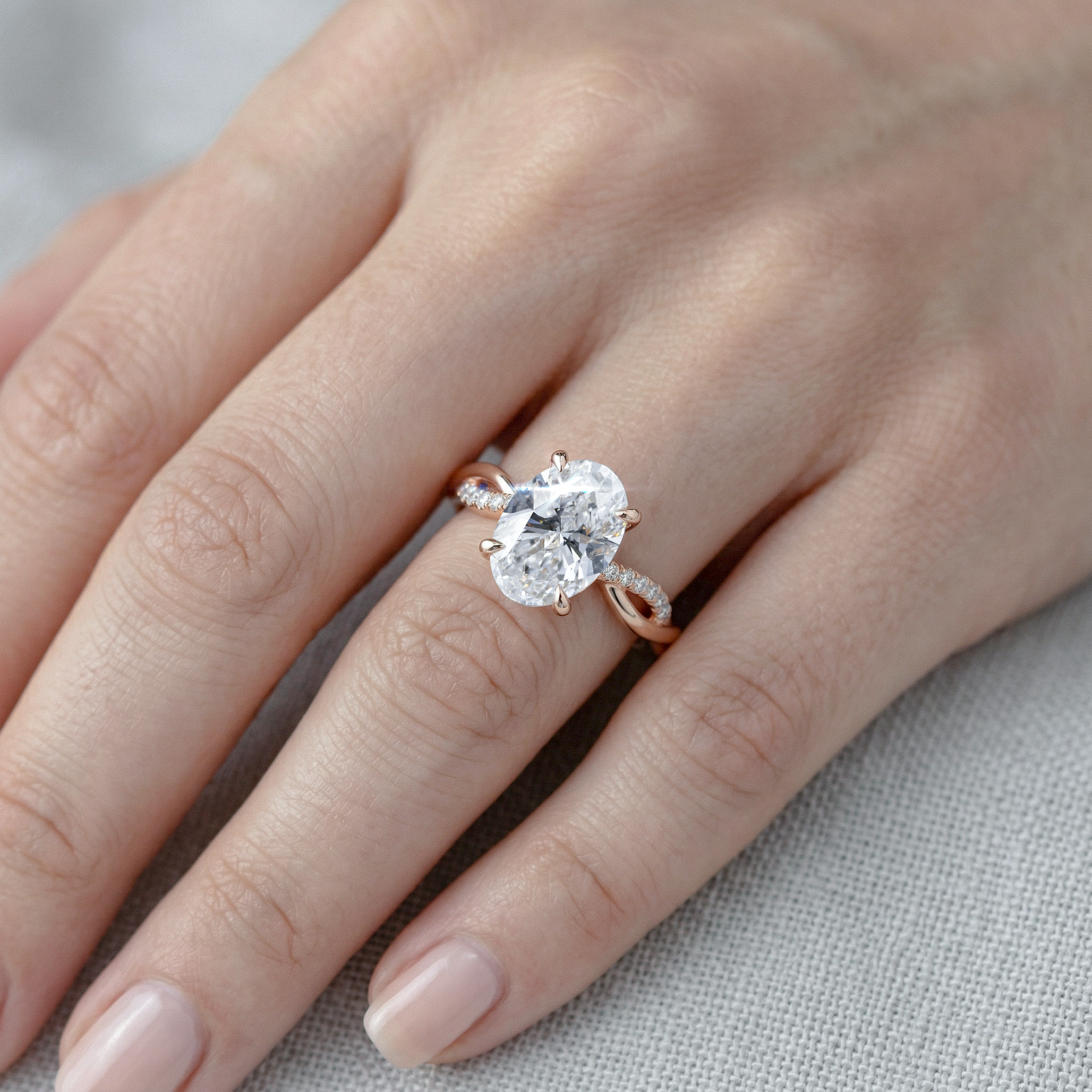 Rose gold twisted ring with a large oval  diamond on a hand against a neutral background