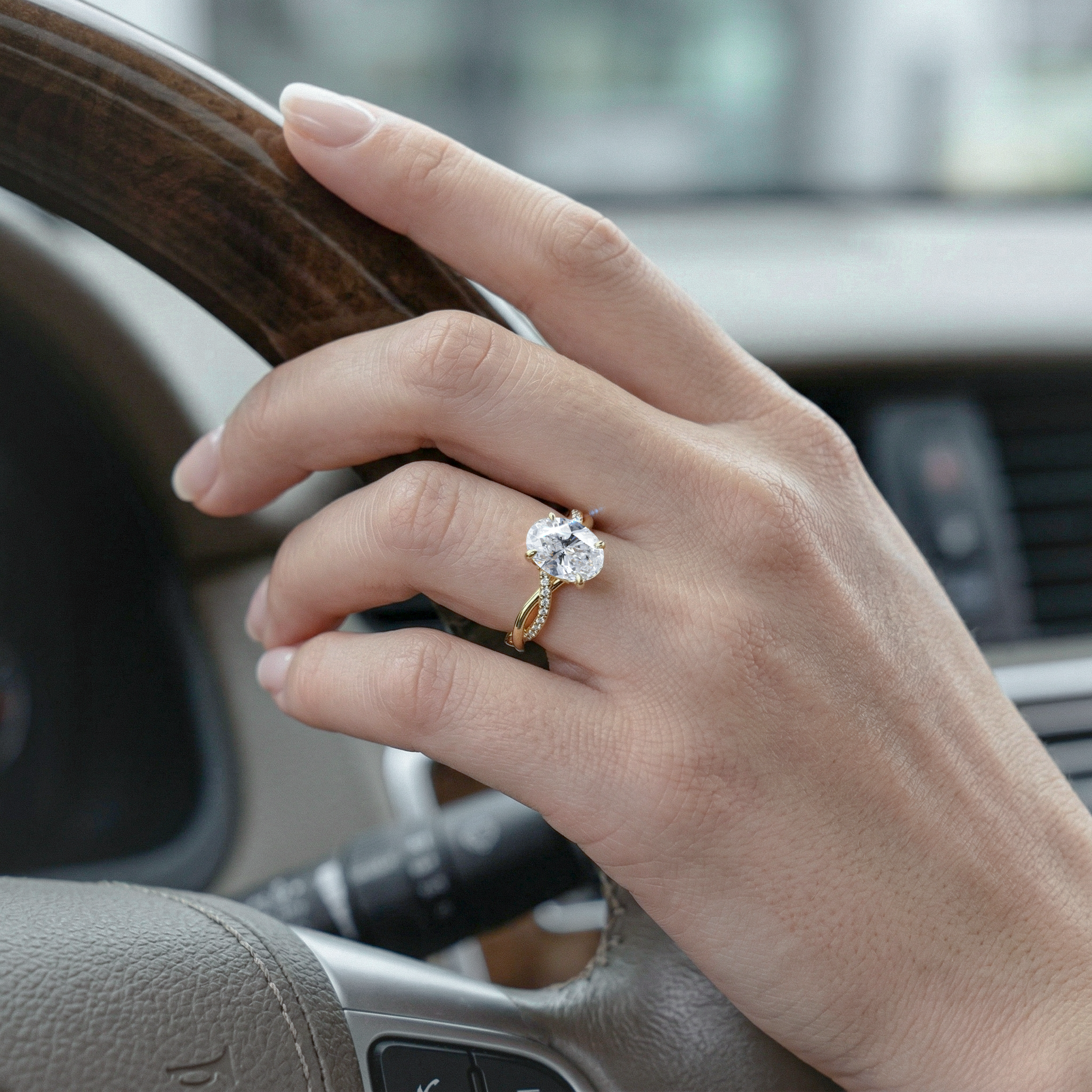 Hand with a golden oval diamond ring on a car steering wheel