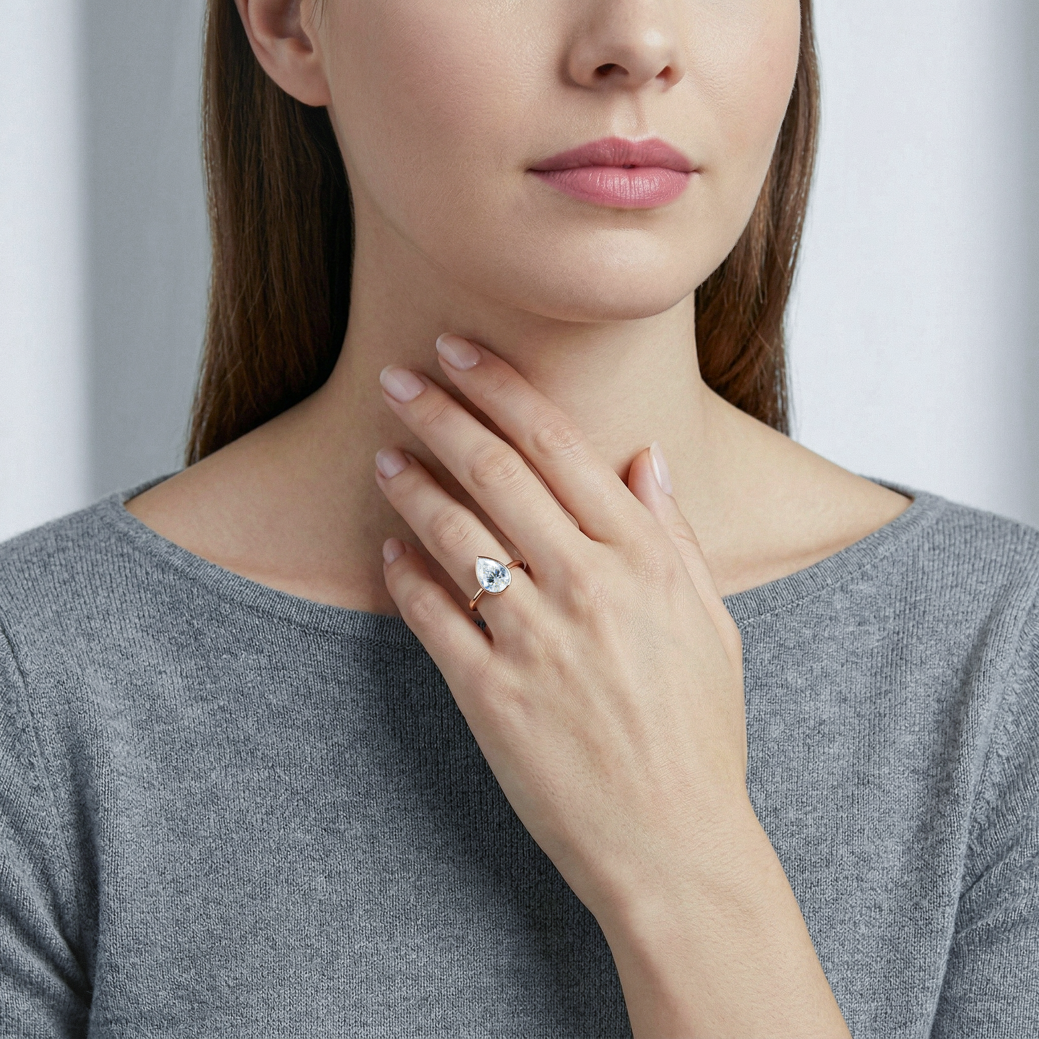Woman wearing sweater with a close-up of her hand bezel pear diamond ring.