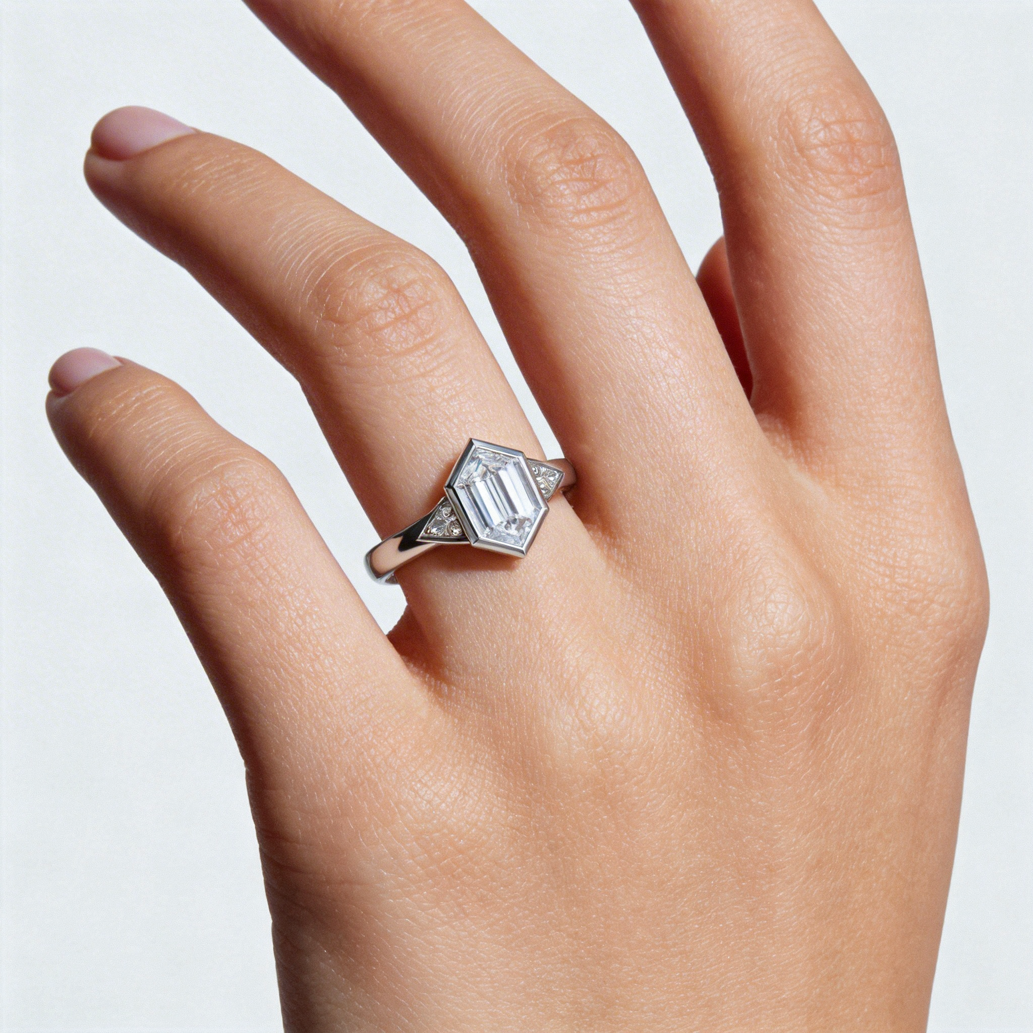 Hand wearing a hexagon diamond ring on a light background