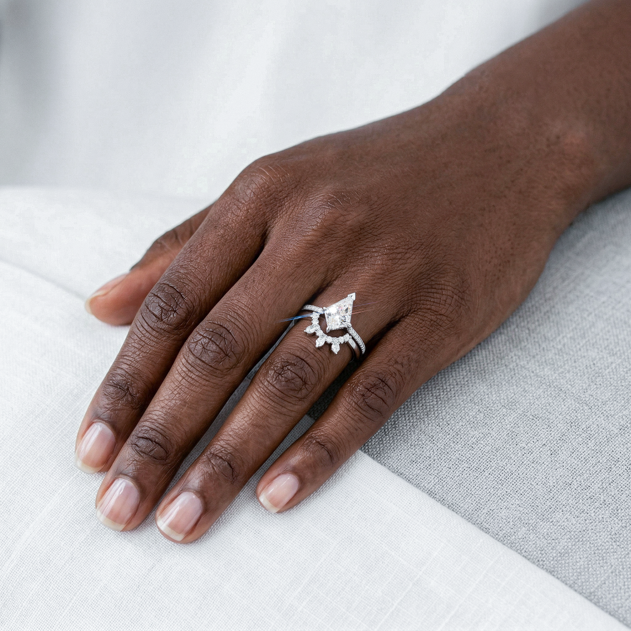 Hand wearing a white gold kite diamond  ring set with a  on a white and gray fabric background