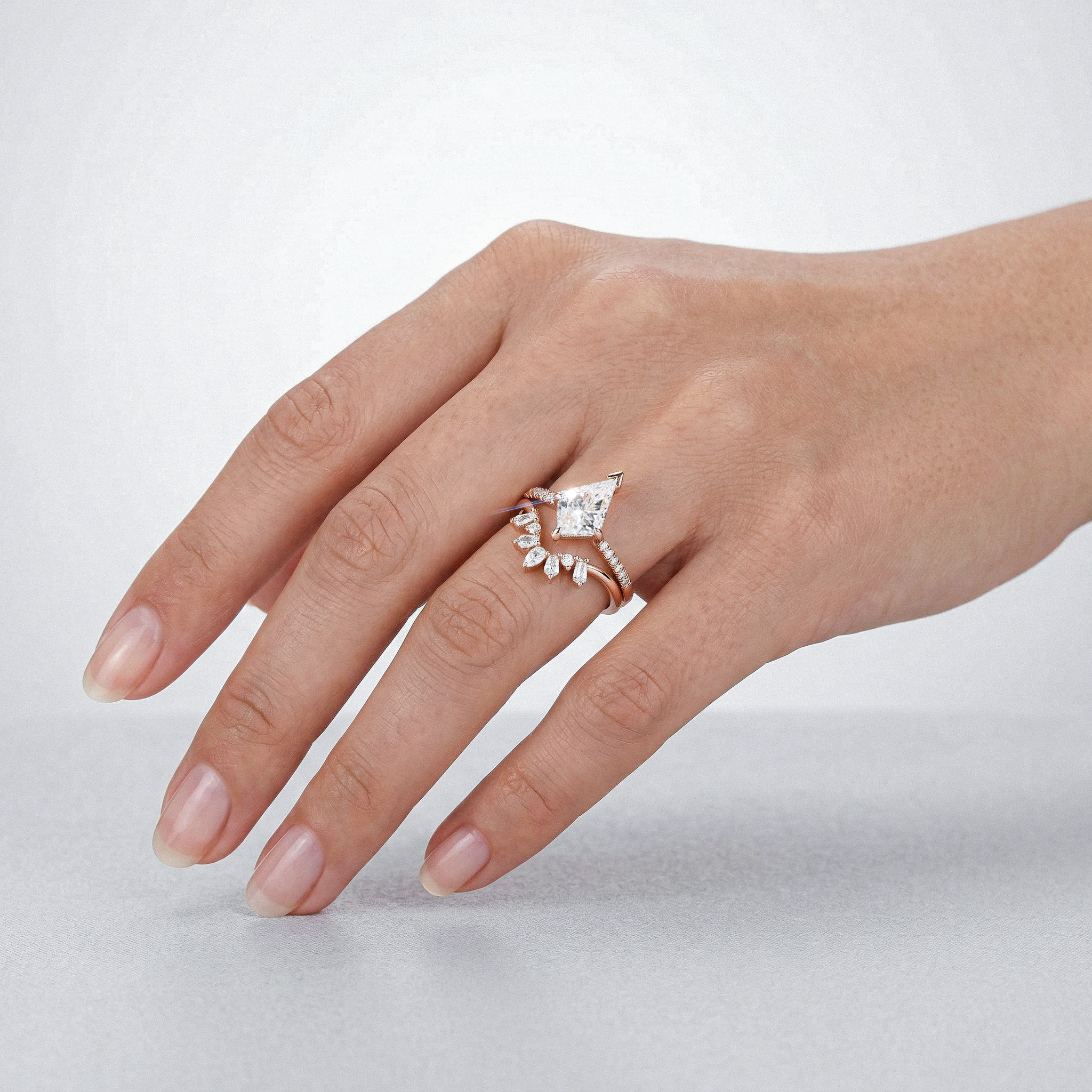 Hand wearing a kite shape diamond ring set on a light gray background