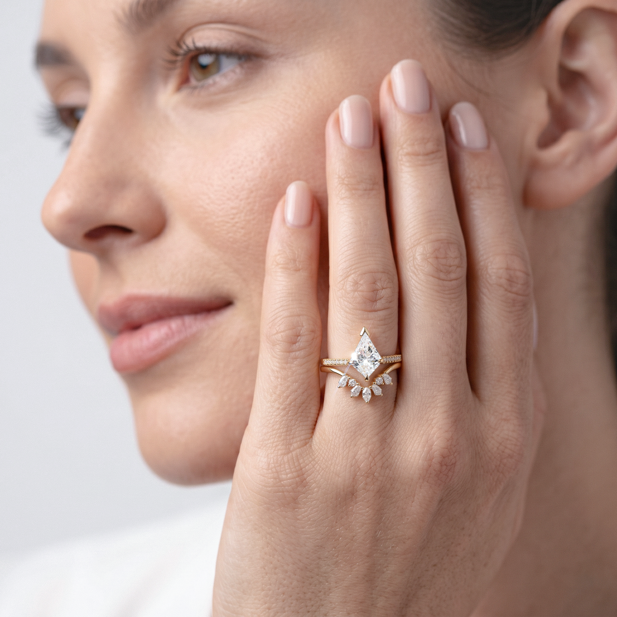 Close-up of a woman's hand wearing kite shape diamond ring set on a light background