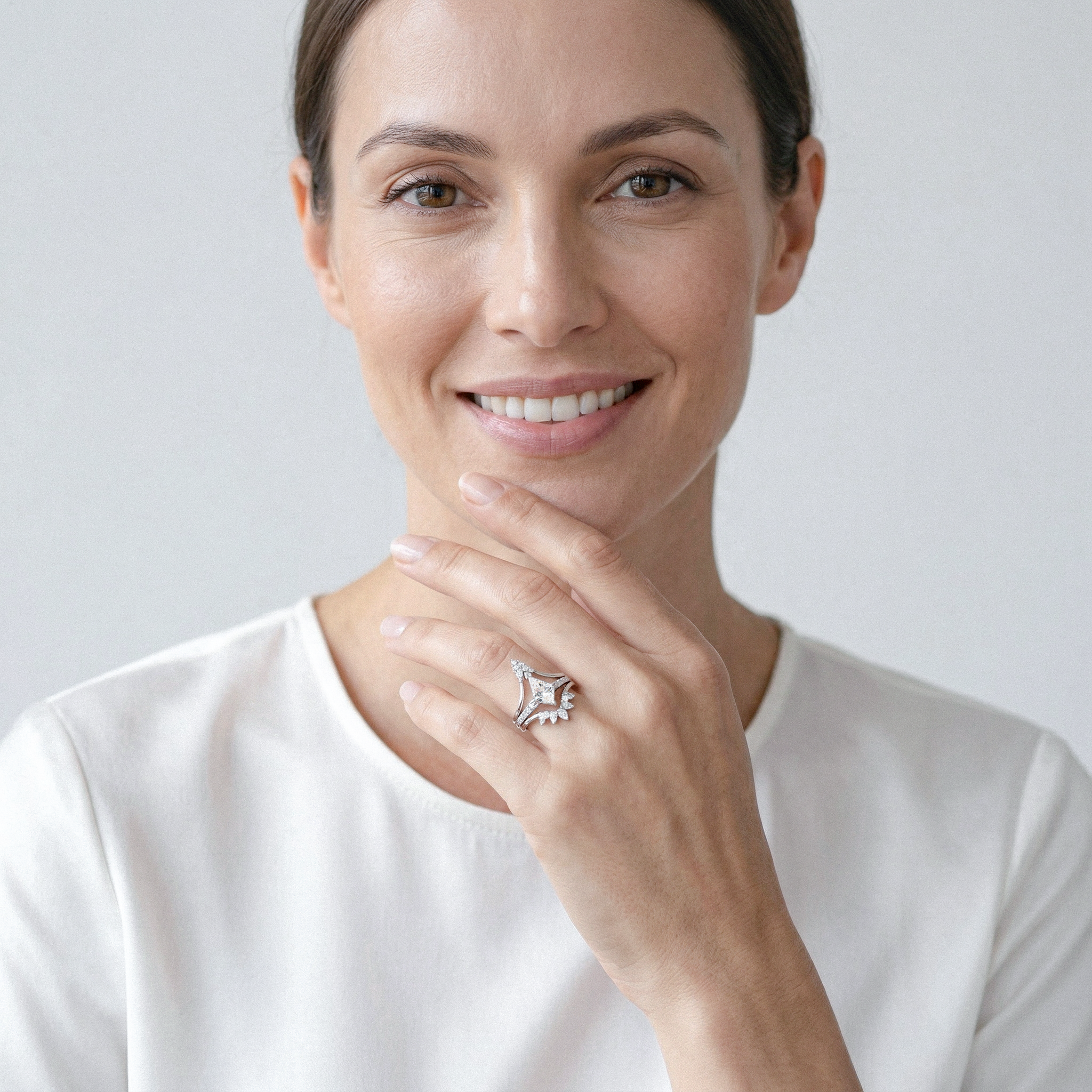 Woman wearing white gold kite shape diamond ring set on a plain background