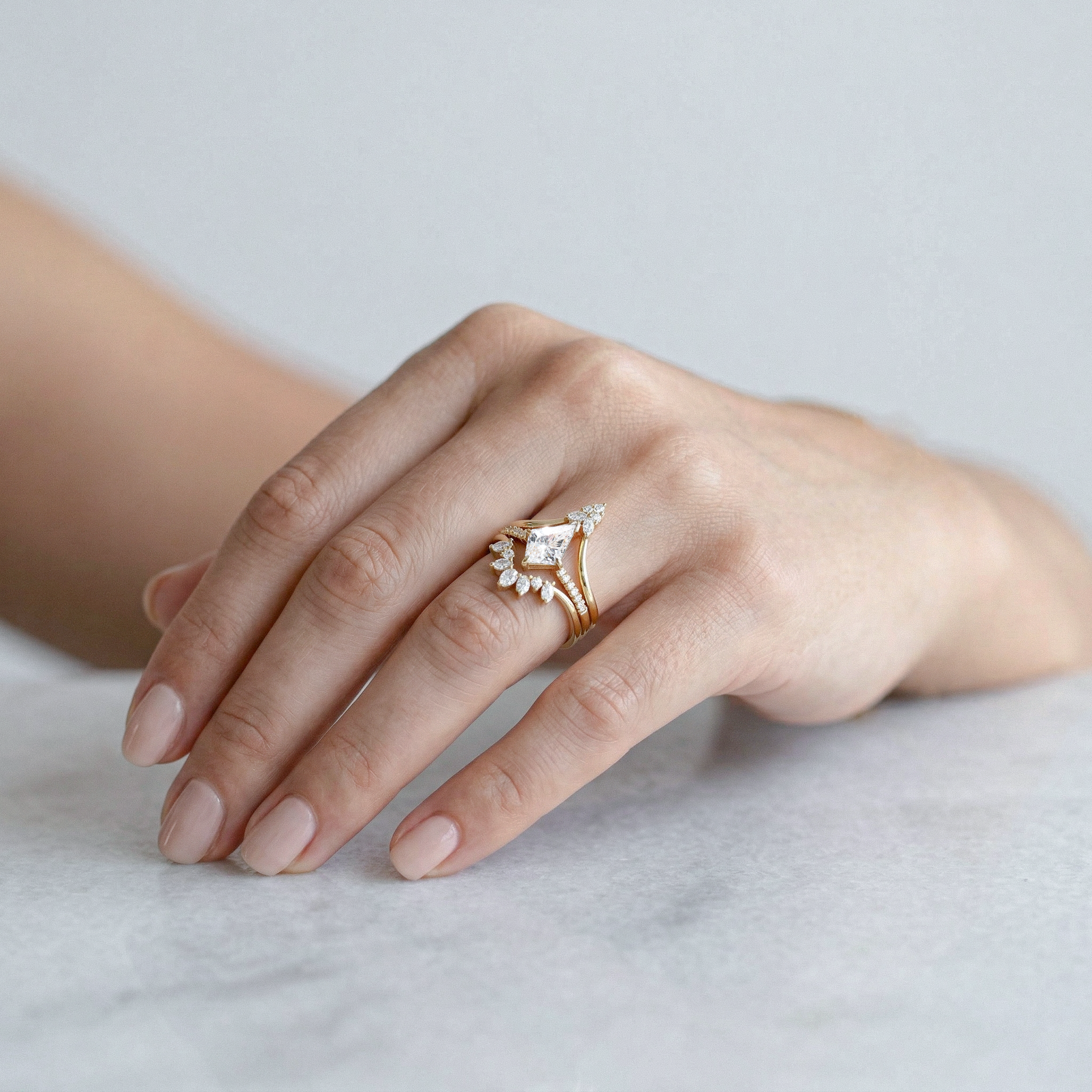 Hand wearing a gold ring with kite shape diamond ring set  on a light background