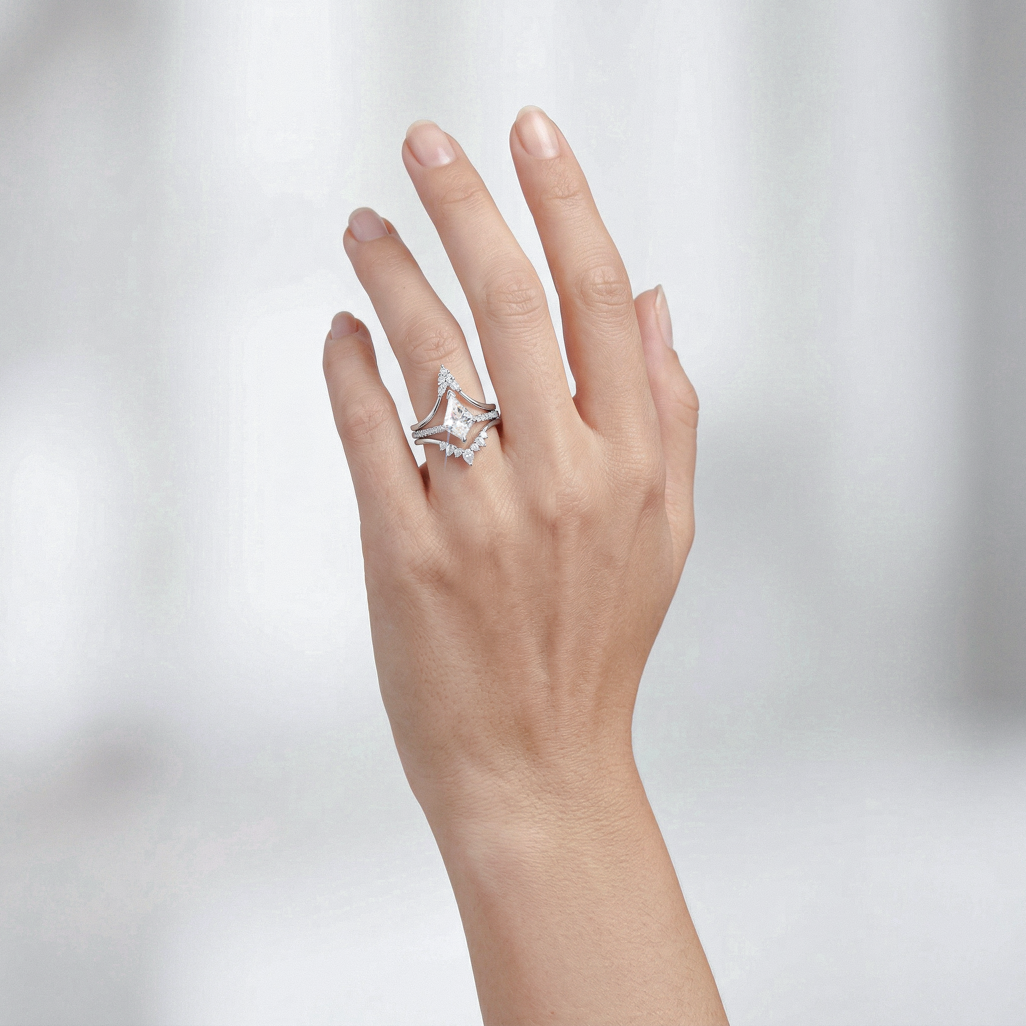 Hand wearing ring set 3piece  with a kite shape diamond on a light gray background