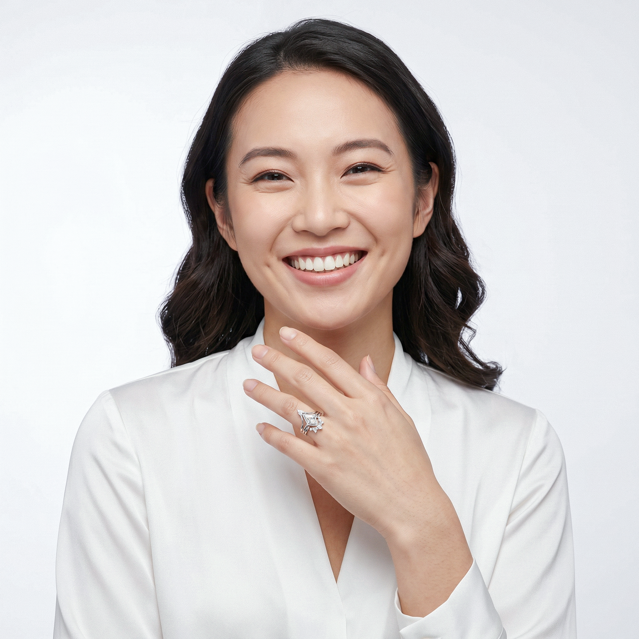 Woman wearing a white shirt and a ring, smiling against a plain background