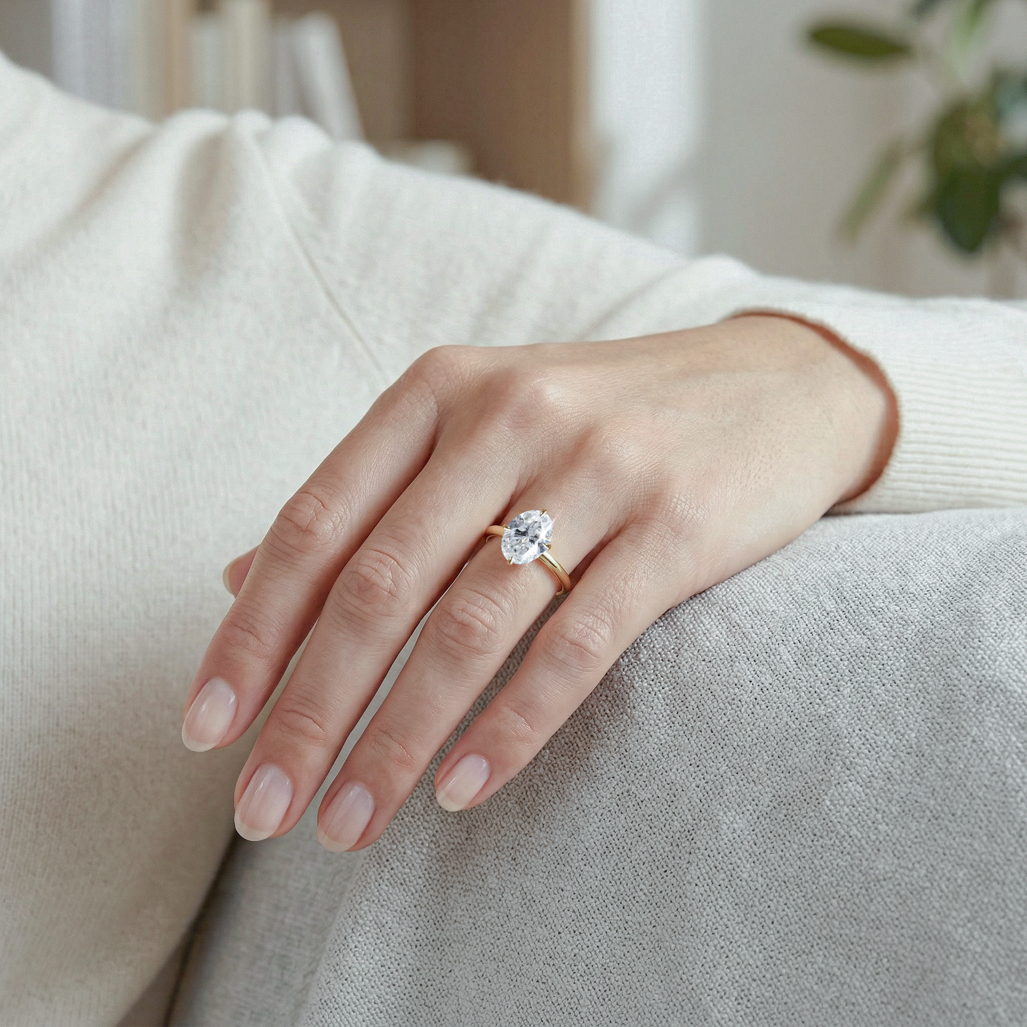 Hand wearing a oval diamond ring on a neutral background