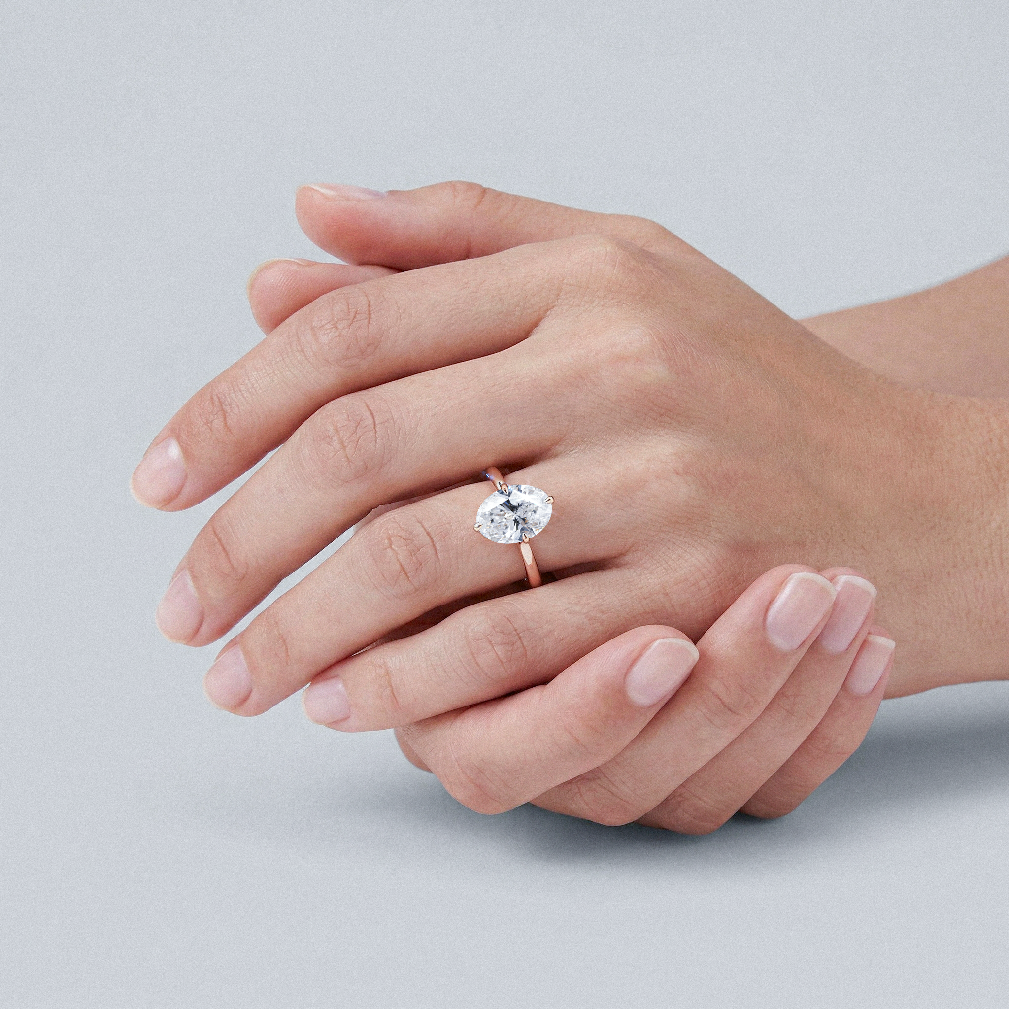 Hand wearing a oval diamond ring on a light gray background