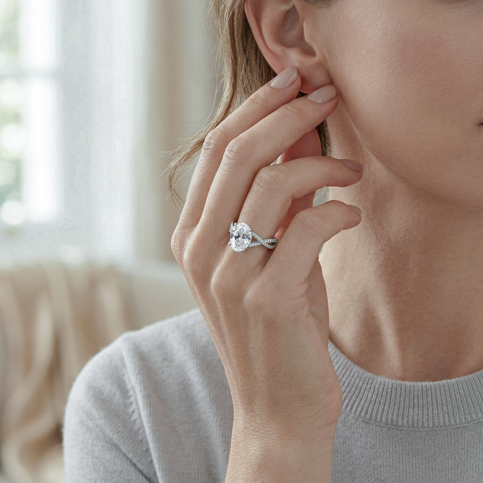Close-up of a woman wearing a gold oval diamond ring on her finger, with a blurred indoor background.