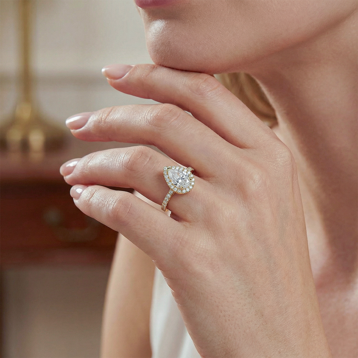 Close-up of a hand wearing a pear cut diamond ring with a blurred background