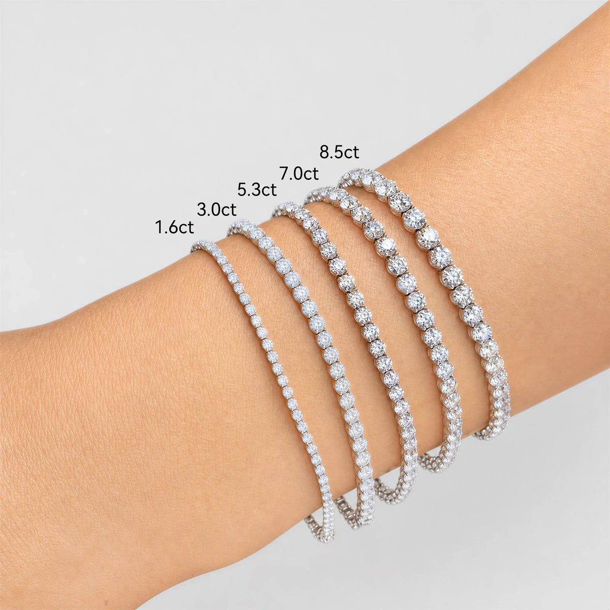 Five white diamond tennis bracelets in graduated carat sizes from 1.6 to 8.5 carats shown on a wrist.